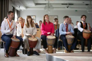 Účastníci teambuildingové akce firmy Atalian hrají na africké bubny djembe během interaktivního workshopu.